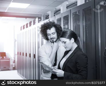 Young IT engineer showing working data center server room to female chief engineer who holding tablet computer