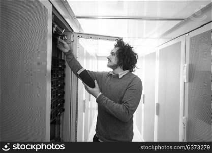 young IT technician using digital cable analyzer on server in large data center