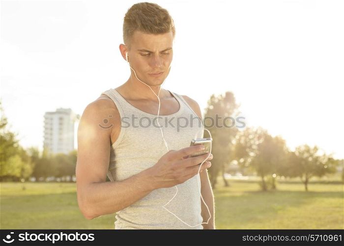Young jogger listening to music through cell phone in park