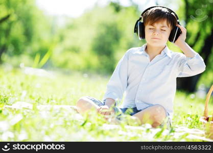 Young joyful boy in summer park wearing headphones. Sounds of nature