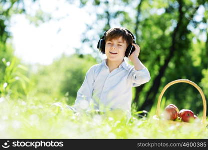 Young joyful boy in summer park wearing headphones. Sounds of nature