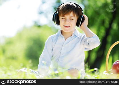 Young joyful boy in summer park wearing headphones. Sounds of nature