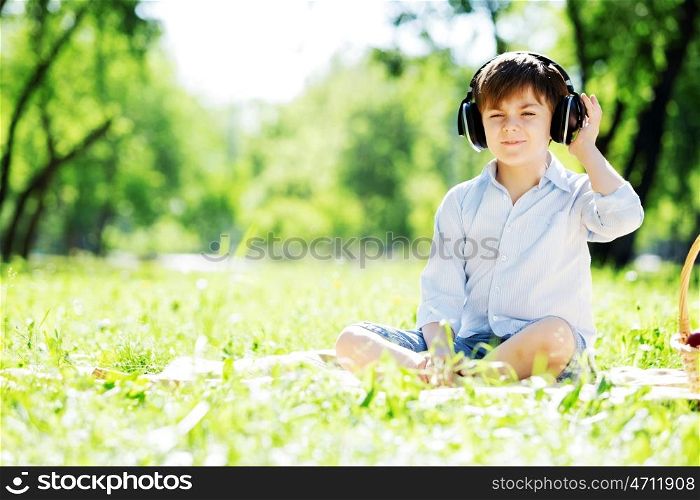 Young joyful boy in summer park wearing headphones. Sounds of nature