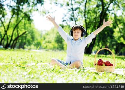 Young joyful boy in summer park wearing headphones. Sounds of nature