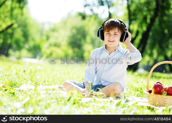 Young joyful boy in summer park wearing headphones. Sounds of nature