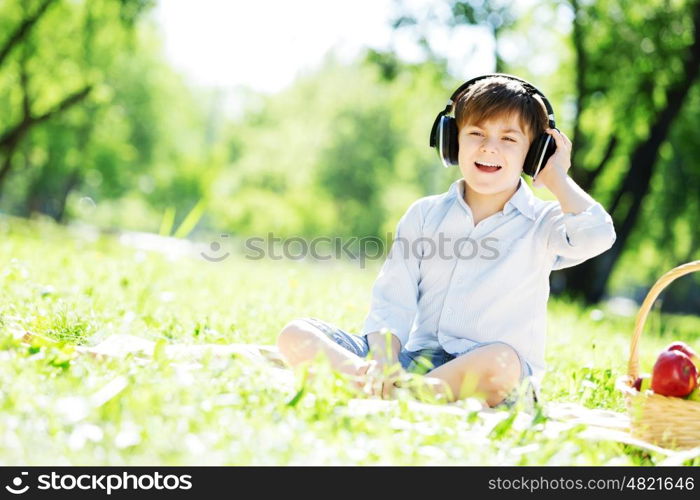 Young joyful boy in summer park wearing headphones. Sounds of nature