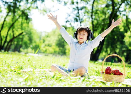 Young joyful boy in summer park wearing headphones. Sounds of nature