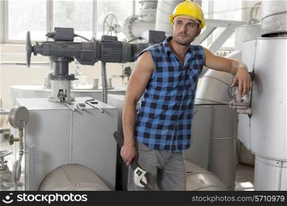 Young labor holding wrench while leaning on industrial machine