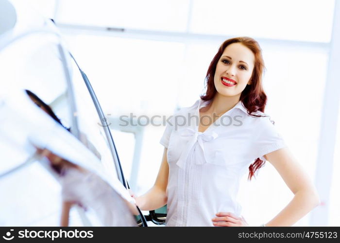 Young lady at car salon. Pretty woman standing near car at car center. Choosing a car