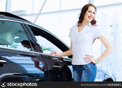 Young lady at car salon. Pretty woman standing near car at car center. Choosing a car