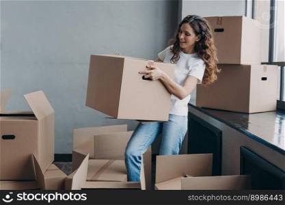 Young lady in white t-shirt is carrying cardboard box. Smiling attractive hispanic woman packing things and leaving. Packed boxes on the floor. Relocation and moving to new apartment concept.. Young lady in white t-shirt is carrying cardboard box. Hispanic woman packing things and leaving.