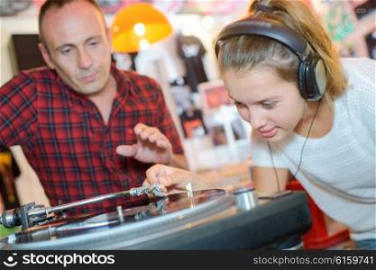 Young lady putting stylus onto record, man urging caution