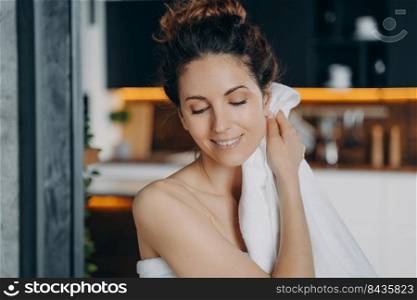 Young lady relaxing in bathroom, enjoying the bath and beauty routine. European girl is wiping face with towel after washing. Woman takes shower at home and doing skin care. Daily hygiene.. Young lady relaxing in bathroom, enjoying the bath and beauty routine. Girl wiping face with towel.