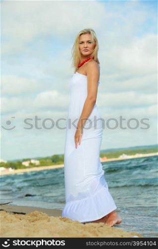 Young lady resting on beach.. Rest and relax concept. Attractive gorgeous blonde woman wearing white dress resting on fresh air on beach seaside. Summer time.