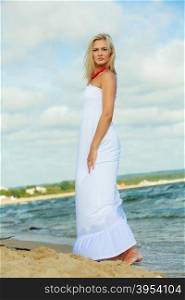 Young lady resting on beach.. Rest and relax concept. Attractive gorgeous blonde woman wearing white dress resting on fresh air on beach seaside. Summer time.