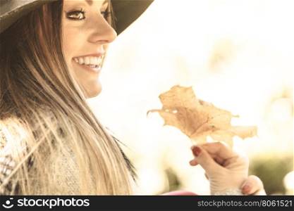 Young lady with leaf outdoor. Seasonal specific. Gorgeous lovely young girl holding gold brown leaf. Beauty trendy woman spending time in autumnal park.
