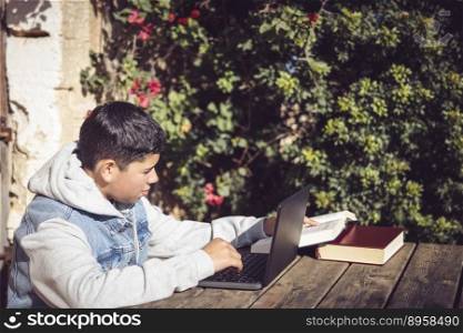 young latin man reads book in front of laptop, outdoors in city park, doing high school study work. young latin man reads book in front of laptop, outdoors