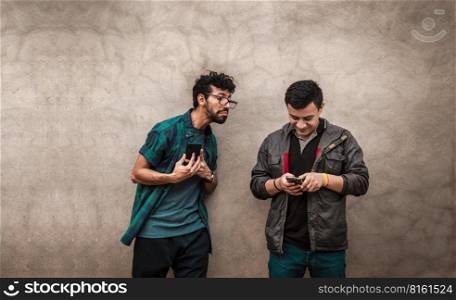 Young latin man spying on another cell phone, man showing his cell phone to another guy