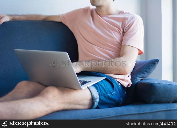 Young latin man using laptop on the cozy sofa at home.