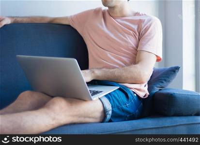 Young latin man using laptop on the cozy sofa at home.