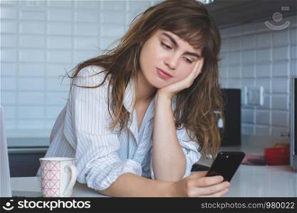 young latin woman in the kitchen with smartphone and coffee