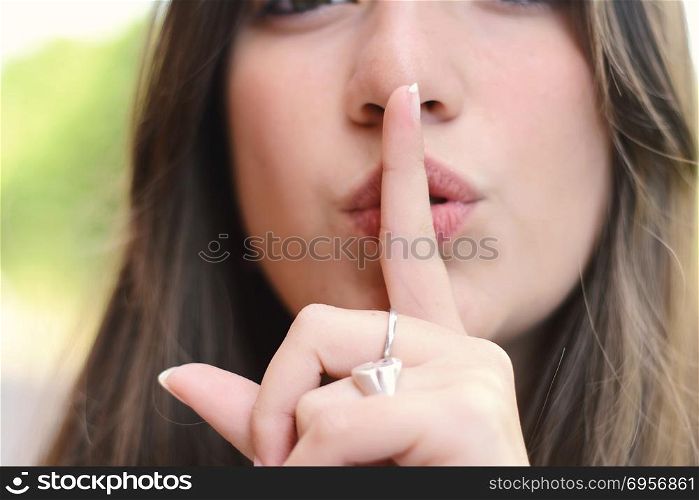 Young latin woman making a quiet gesture with finger on her lips. Outdoors.. Happy young woman making a quiet gesture