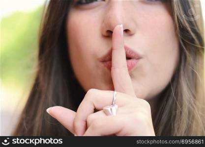 Young latin woman making a quiet gesture with finger on her lips. Outdoors.. Happy young woman making a quiet gesture