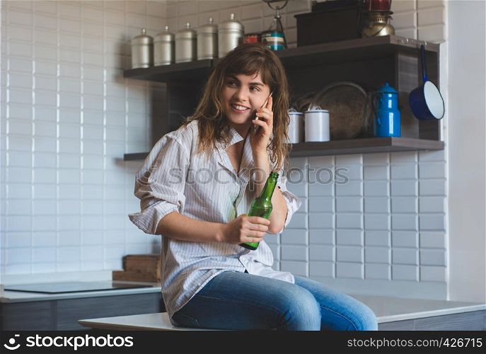Young latin woman talking on mobile phone and drinks beer at home.