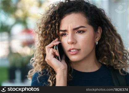 Young latin woman talking on the phone while standing outdoors in the street. Urban concept.