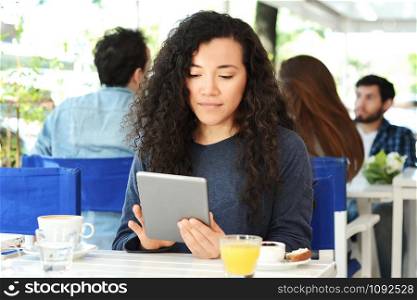 Young latin woman using digital tablet in coffee shop.
