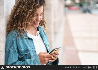 Young latin woman using her mobile phone while standing outdoors on the street. Urban concept.
