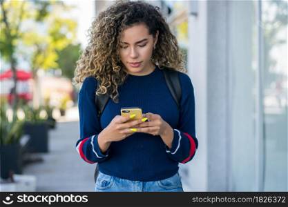Young latin woman using her mobile phone while walking outdoors on the street. Urban concept.