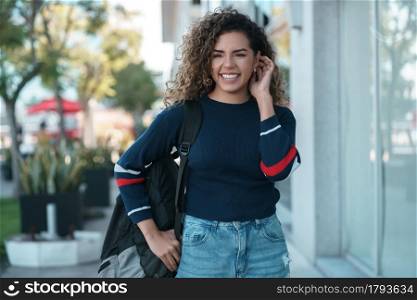 Young latin woman with curly hair smiling while walking outdoors on the street. Urban concept.