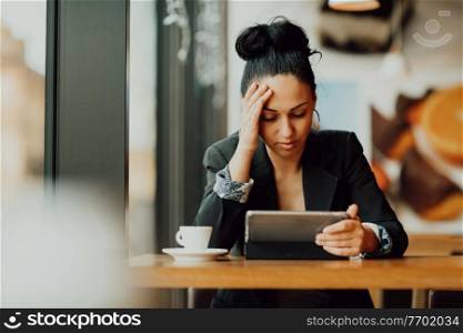 Young Latin woman with sad face sitting in the coffee shop at wooden table, drinking coffee and using a laptop.. a Latina woman sits in a cafe and looks in disappointment at the tablet