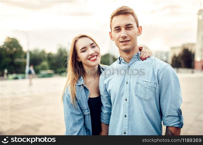 Young laughing couple hugs in summer city park. Smiling teenagers poses together, cityscape on background