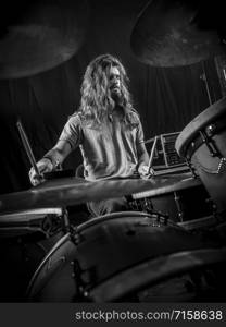 Young long-haired drummer playing his drum set during a concert.