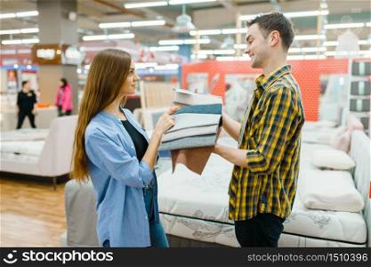 Young love couple choosing texture of mattress in furniture store showroom. Man and woman looking samples for bedroom in shop, husband and wife buys goods for modern home interior. Couple choosing texture of mattress in store