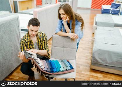 Young love couple choosing texture of mattress topper in furniture store showroom. Man and woman looking samples for bedroom in shop, husband and wife buys goods for modern home interior. Love couple choosing texture of mattress topper