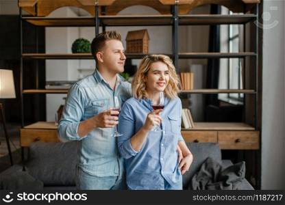 Young love couple drinks red wine, romantic dinner. Man and woman relaxing in living room. Happy lifestyle, beautiful relationship