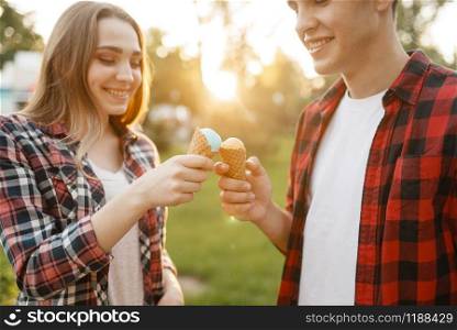 Young love couple feed each other ice cream in summer park. Boyfriend and girlfriend leisures together with ice-cream, romantic walk. Couple feed each other ice cream in summer park
