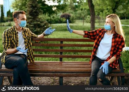Young love couple in masks and gloves sitting on bench in park, quarantine. Romantic meeting during the epidemic, health care and protection, pandemic lifestyle. Love couple in masks sitting on bench, quarantine.