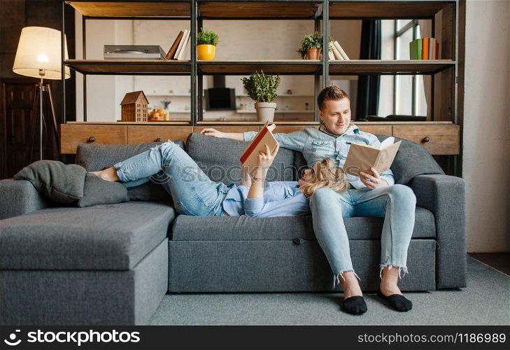 Young love couple resting on comfortable couch at home. Husband and wife relax in living room. Happy family together, man and woman reading books on sofa. Love couple resting on comfortable couch at home