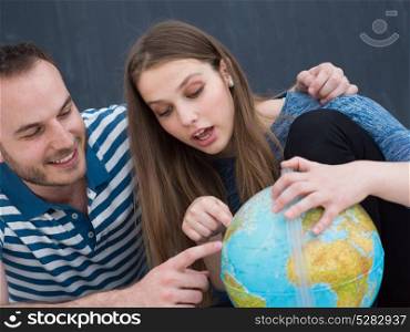 Young lovely couple in casual clothing investigating globe isolated over gray background