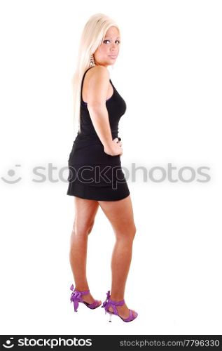 Young, lovely girl in a black dress and long blond hair, in high pink heels standing in the studio for white background.