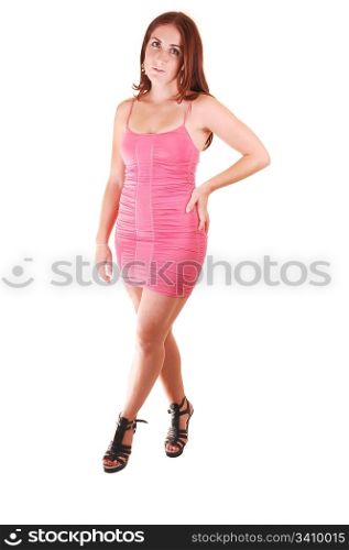 Young, lovely girl in a short pink dress with red hair, looking in the camera, on high heels standing in the studio for white background.