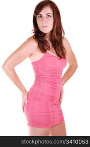 Young, lovely girl in a short pink dress with red hair, looking in the cameraholding her butt, standing in the studio for white background.