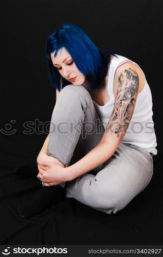 Young lovely girl in gray blue jeans and white T-Shirt, sitting on the floor and dreaming, with a nice tattoo on her arm, for black background.