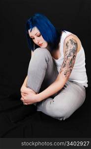 Young lovely girl in gray blue jeans and white T-Shirt, sitting on the floor and dreaming, with a nice tattoo on her arm, for black background.