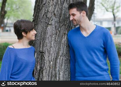 Young lovers dressed in blue supported on a tree at the park