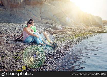 Young lovers sitting near water and looking away in sunbeams